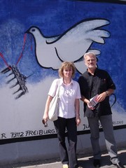 Mann und Frau vor einer Mauer, auf die eine Friedenstaube gesprüht ist.